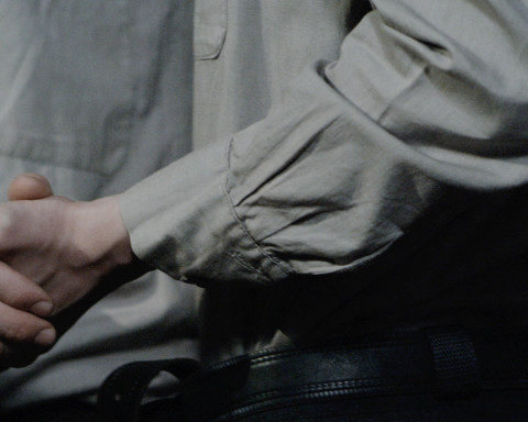 A still from Polina Kanis' "Celebration" which shows two figures shaking hands with both figures wearing grey clothing